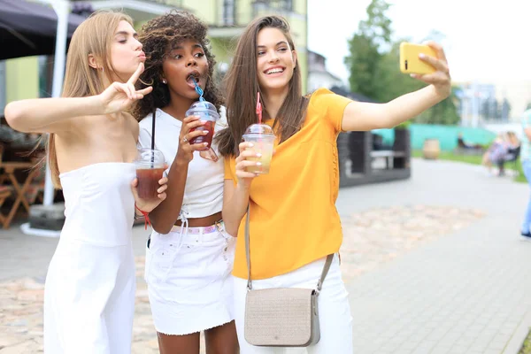 Trois filles branchées cool hipster, amis boire un cocktail et prendre selfie en arrière-plan de la ville . — Photo