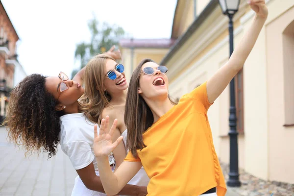 Três bonitos jovens amigas se divertindo juntas, tirando uma selfie na cidade . — Fotografia de Stock