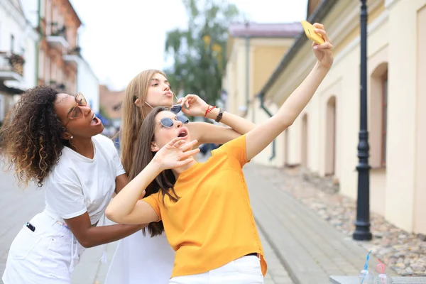 Tres amigas jóvenes lindas divirtiéndose juntas, tomando una selfie en la ciudad . — Foto de Stock