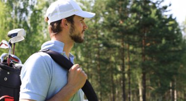 Golf oyuncusu yaz golfü sırasında yolda yürüyor ve çanta taşıyor..