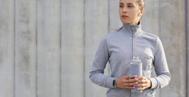 Güzel bayan koşucu elinde su şişesiyle dışarıda duruyor. Spor yaptıktan sonra spor yapan kadın ara veriyor.