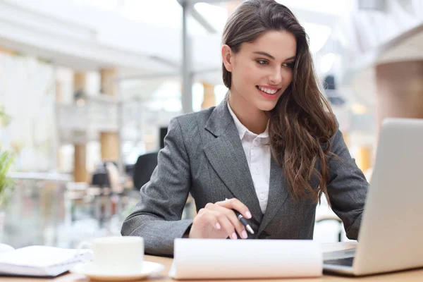 Portrait d'une jeune femme d'affaires brune utilisant un ordinateur portable au bureau. — Photo