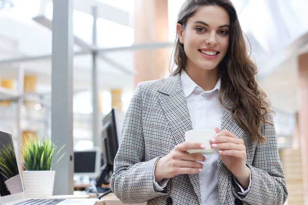 Belle femme d'affaires souriante debout dans le bureau avec une tasse de café . — Photo