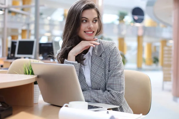 Portrait d'une jeune femme d'affaires brune utilisant un ordinateur portable au bureau. — Photo