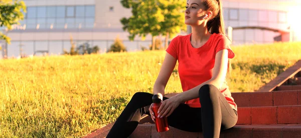 Привлекательная молодая женщина в спортивной одежде отдыхает сидя на лестнице с вечерним солнечным светом . — стоковое фото