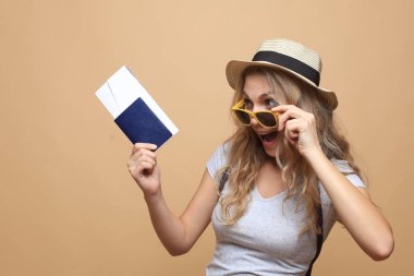 Güneş gözlüklü, pasaportlu, bej arka planda biletleri olan güzel sarışın kadın..