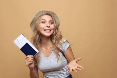 Yazlık kıyafetler giyen güzel sarışın kadın. Bej arka planda biletleri olan pasaport ile poz veriyor..