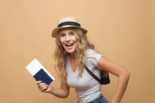 Mooie blonde vrouw in de zomer kleding poseren met paspoort met tickets over beige achtergrond. — Stockfoto