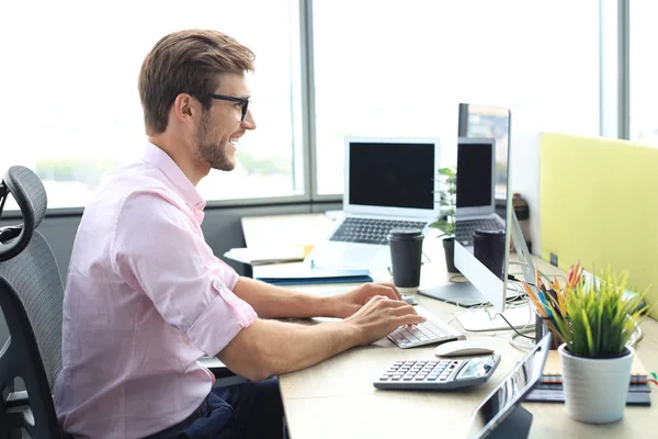 Pensativo joven hombre de negocios en camisa de trabajo utilizando la computadora mientras está de pie en la oficina . — Foto de Stock