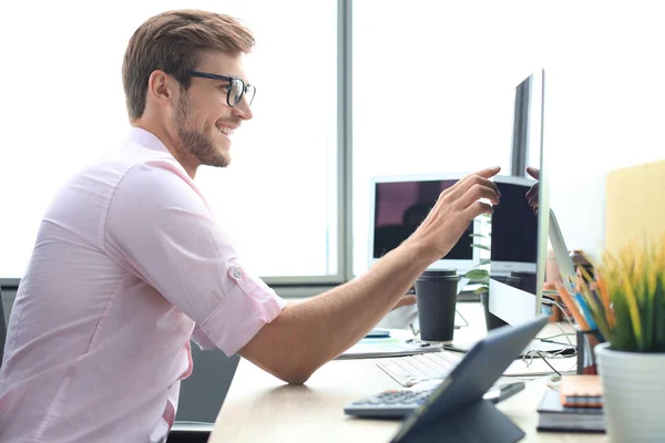 Figyelmes fiatal üzletember ingben, aki számítógéppel dolgozik, miközben az irodában áll. — Stock Fotó