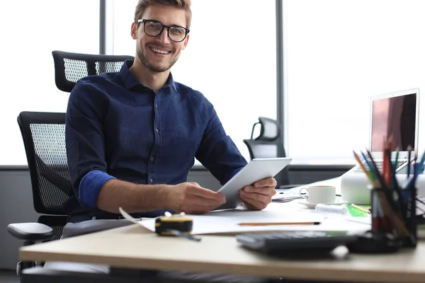 Mladý moderní podnikatel pracující pomocí digitálního tabletu, zatímco sedí v kanceláři. — Stock fotografie