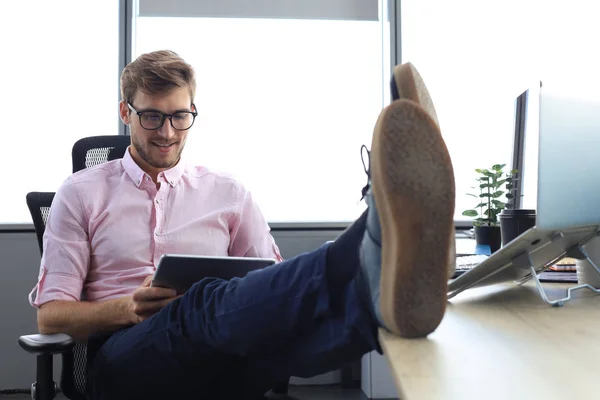 Nowoczesny biznesmen pracujący z tabletem cyfrowym w nowoczesnym biurze, nogi na biurku. — Zdjęcie stockowe