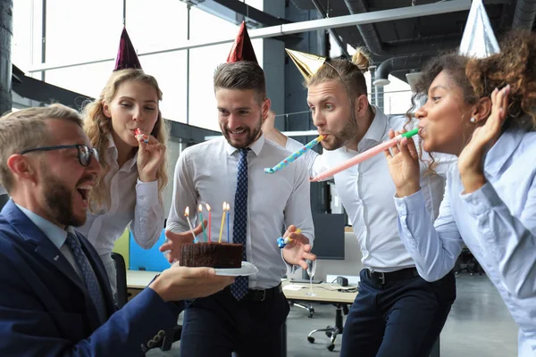 Happy business team with birthday cake are greeting colleague at office party