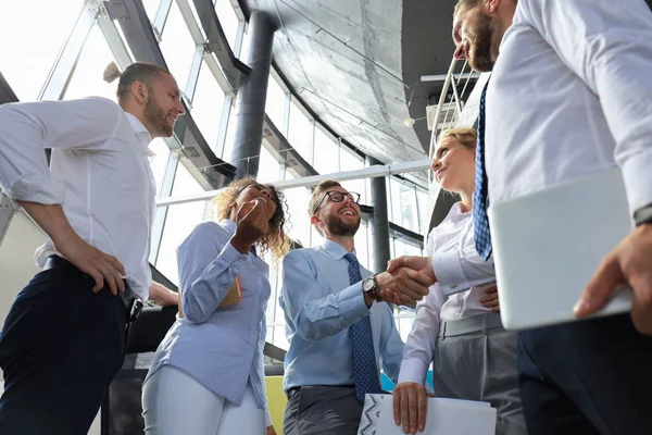 Dois empresários sorridentes estão apertando as mãos enquanto estão no cargo junto com seus colegas — Fotografia de Stock