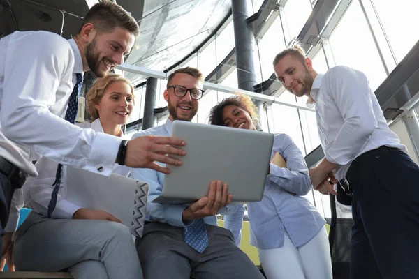 Groupe de gens d'affaires modernes utilisant un ordinateur portable et souriant tout en se tenant dans le bureau . — Photo