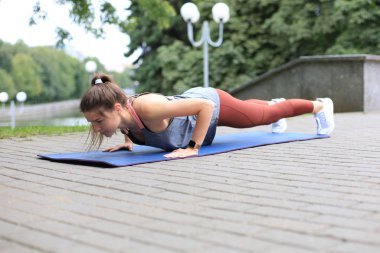 Formda genç bir kadın parkta tahta egzersizi yapıyor..