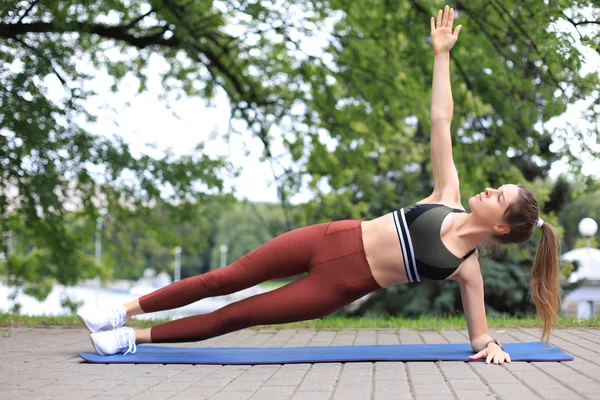 Ung fitness kvinna i sportkläder gör sidoplanka motion utomhus. — Stockfoto