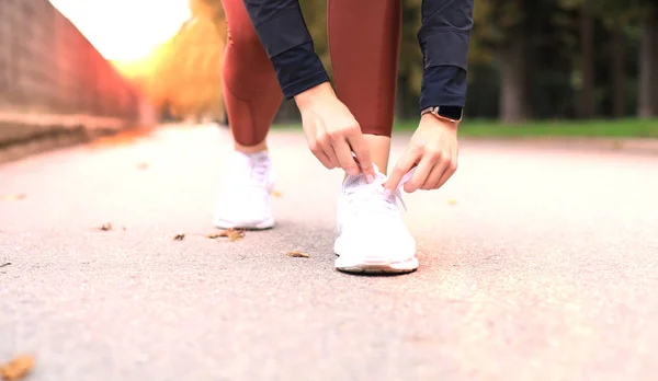 Closeup of unrecognizable sport woman tying sports shoes during evening run outdoors. — Stock Photo, Image