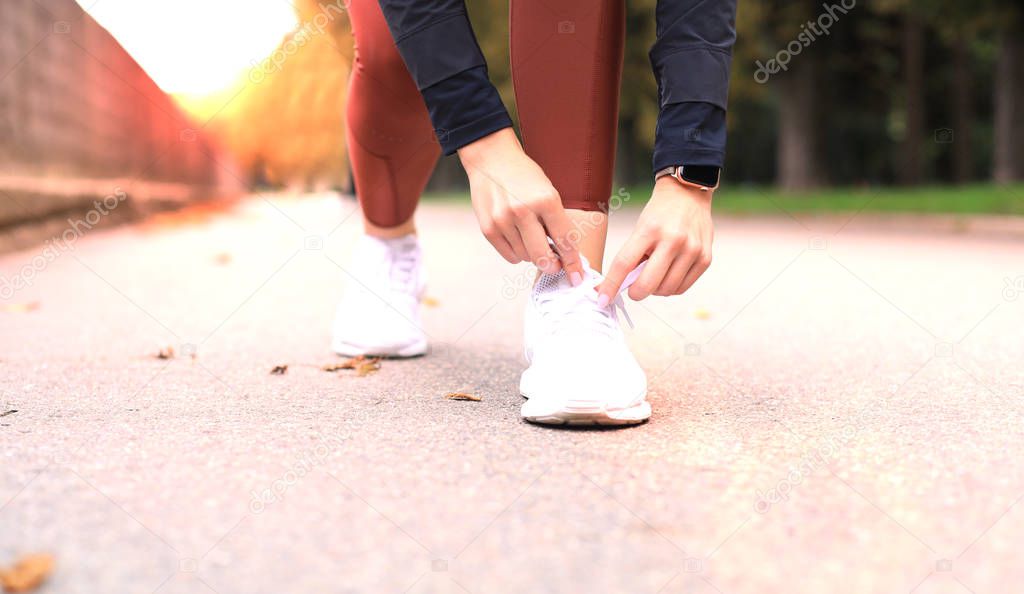 Closeup of unrecognizable sport woman tying sports shoes during evening run outdoors.