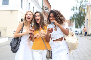 Üç popüler havalı hippi kız, arkadaşlar şehir arka planında kokteyl içiyorlar..