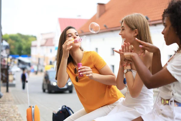 Três mulheres bonitas felizes soprando bolhas de sabão na rua da cidade . — Fotografia de Stock