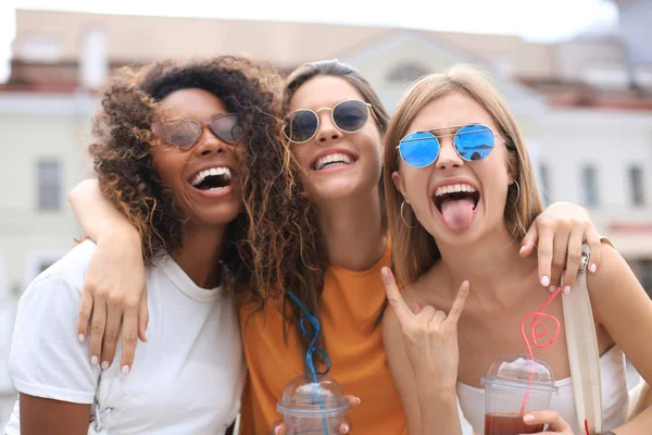 Tre unga leende hipster kvinnor i sommarkläder poserar på gatan.Kvinna visar positiva ansiktskänslor. — Stockfoto