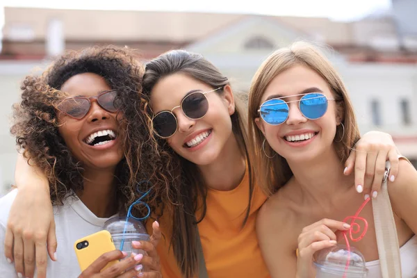 Tre ragazze alla moda cool hipster, gli amici bevono cocktail in città urbana sfondo. — Foto Stock