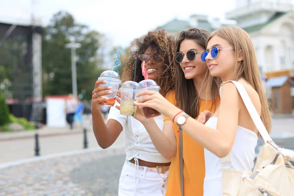 Três meninas hipster cool na moda, amigos bebem coquetel no fundo da cidade urbana. — Fotografia de Stock