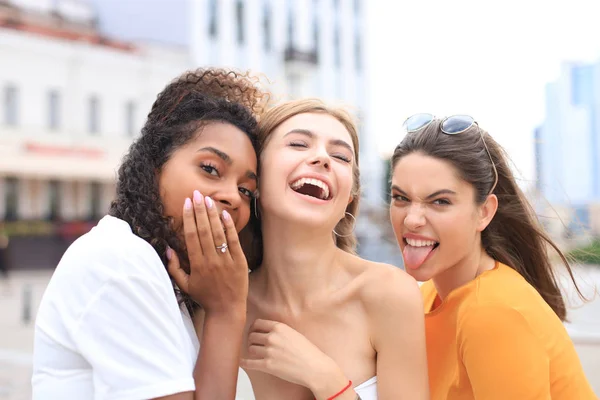 Tři mladé usmívající se hipster ženy v letních šatech pózují na ulici.Žena ukazuje pozitivní tvář emoce. — Stock fotografie