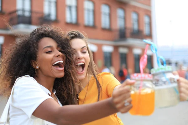 Divatos hűvös hipster lányok, barátok koktélt isznak városi háttérben. — Stock Fotó