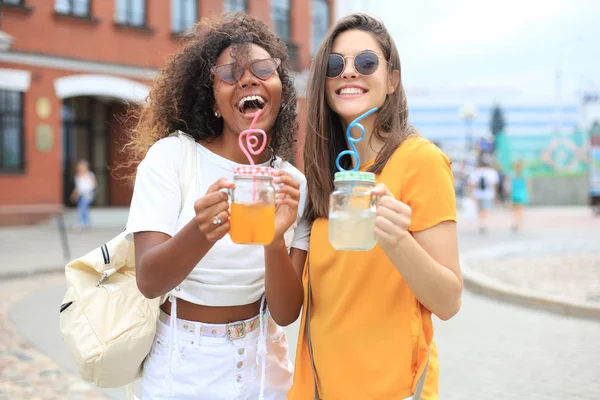 Modne hipsterskie dziewczyny, przyjaciele piją koktajl w miejskim tle. — Zdjęcie stockowe