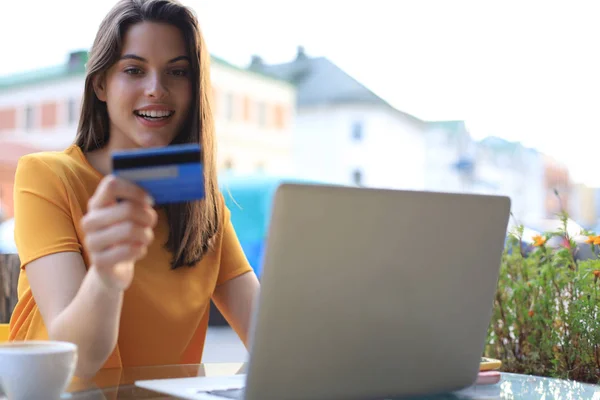 Feliz morena natural con tarjeta de crédito y portátil en la cafetería al aire libre . — Foto de Stock
