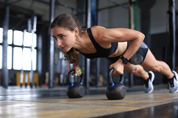 Retrato de una mujer musculosa en posición de tablón con kettlebell en el gimnasio . — Foto de Stock