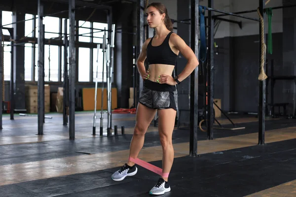 Muskulös och stark flicka gör övningar använda fitness gummi på gym. — Stockfoto