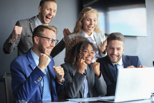 Öt boldog modern üzletember emeli fel a karját és fejezi ki örömét, miközben a laptop mellett ül az irodában.. — Stock Fotó