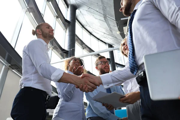 Dois empresários sorridentes estão apertando as mãos enquanto estão no cargo junto com seus colegas — Fotografia de Stock