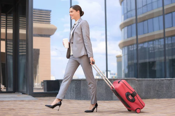 Açık havada yürürken bavul çekerek takım elbise li giden başarılı iş kadını portresi. — Stok fotoğraf