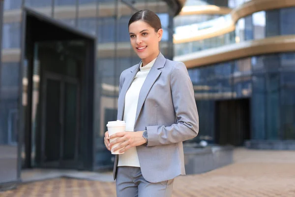 Portrait d'une femme d'affaires prospère allant travailler avec un café marchant près d'un immeuble de bureaux dans la rue de la ville. — Photo