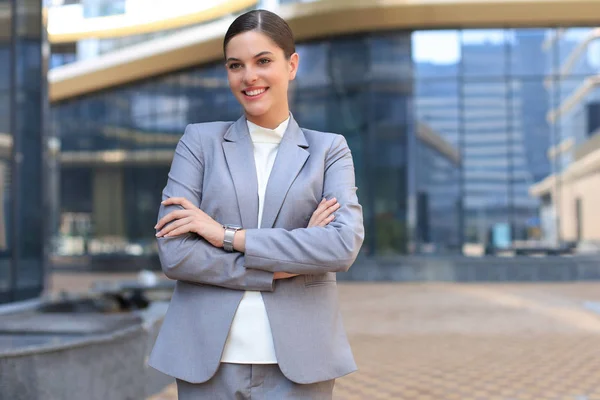 Mujer joven atractiva en traje mirando a la cámara y sonriendo mientras está de pie al aire libre. — Foto de Stock