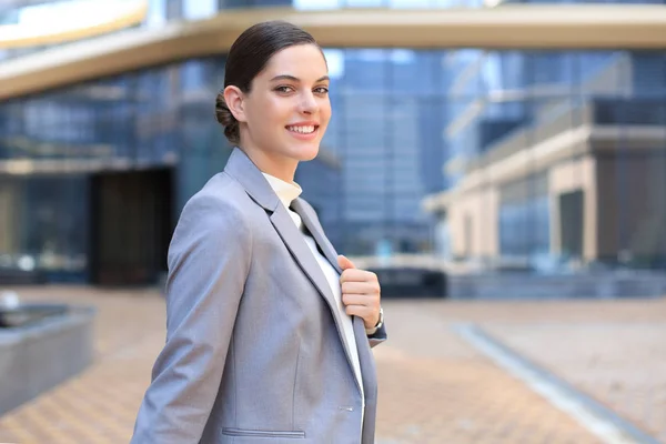 Attractive young woman in suit looking at camera and smiling while standing outdoors. — Stock Photo, Image