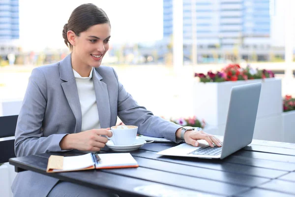 Portrait de femme d'affaires réussie utilisant un ordinateur portable et souriant tout en étant assis dans un café, en plein air . — Photo