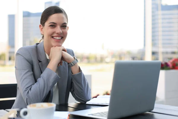 Portrait de femme d'affaires réussie utilisant un ordinateur portable et souriant tout en étant assis dans un café, en plein air . — Photo