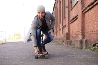 Şehirde sokakta uzun tahta üzerinde gri ceket ve şapka yakışıklı genç adam. Kentsel kaykay konsepti.