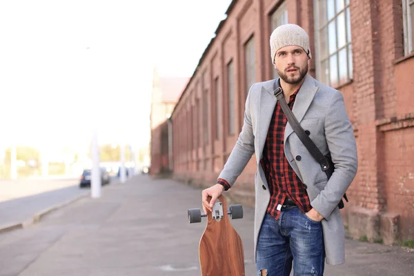 Όμορφος νέος άντρας με γκρι παλτό και καπέλο που περπατάει στο δρόμο, χρησιμοποιώντας παρασανίδα. — Φωτογραφία Αρχείου