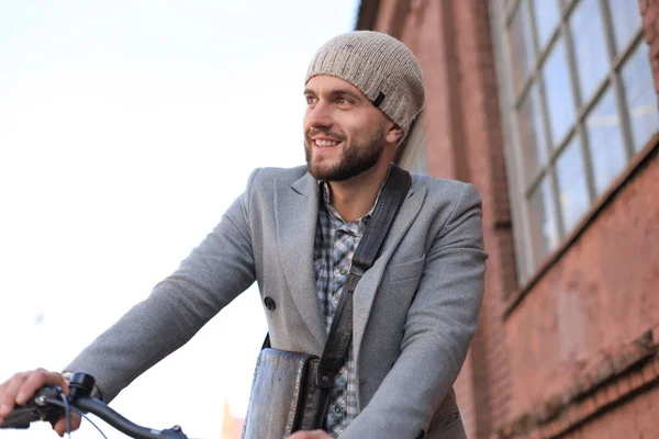 Joven guapo con abrigo gris y sombrero de pie con su bicicleta . — Foto de Stock