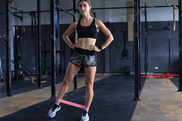 Gespierd en sterk meisje doen oefeningen gebruik fitness rubber in de sportschool. — Stockfoto