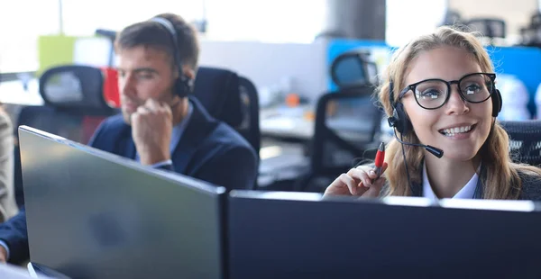 Operatore di assistenza clienti femminile con auricolare e sorridente, con collegi sullo sfondo. — Foto Stock