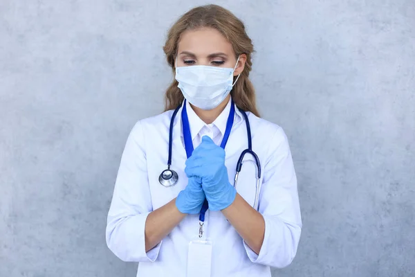 Woman doctor in a mask with closed eyes praying isolated on gray background. — 스톡 사진