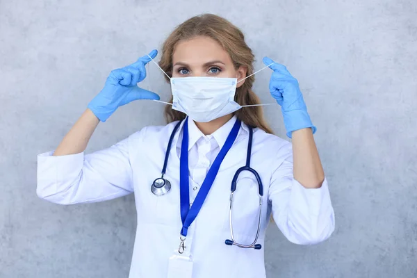 Žena lékař v lékařské masce se stetoskopem při pohledu na kameru izolované přes šedé pozadí. — Stock fotografie