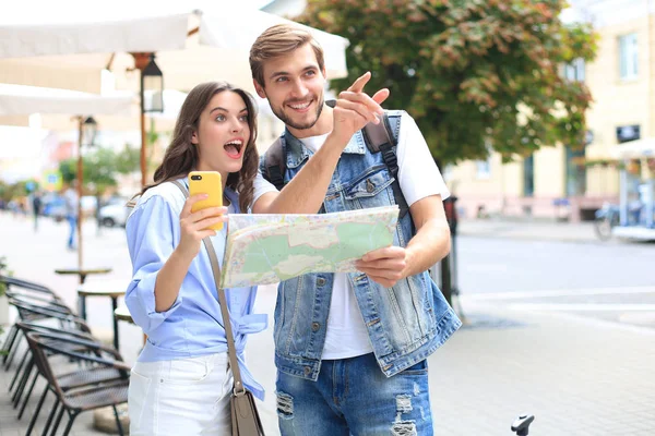 Beau jeune couple tenant une carte et souriant tout en se tenant à l'extérieur. — Photo